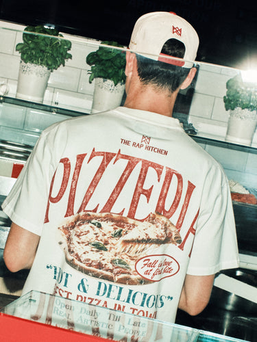 Person wearing a 'PIZZEDIA' t-shirt in a kitchen setting with a counter and appliances.